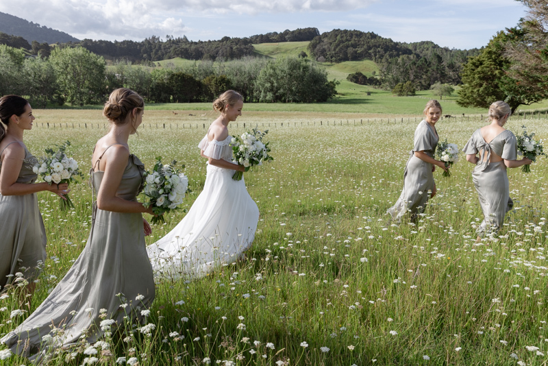 Bride and bridesmaids walking through long grass at St Clair Farm wedding venue in Whangārei, Northland
