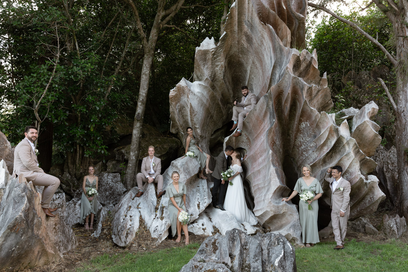 Bridal party standing in front of St Clair Farm's iconic rock formation while the bride and groom share a kiss.